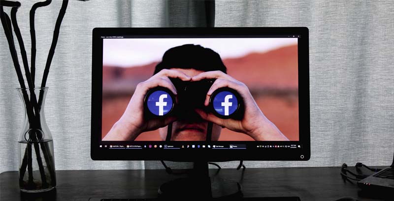 laptop con la imagen de un hombre con binaculares con el logo de facebook en cada lente